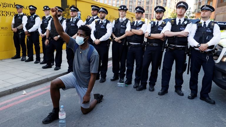 A man wearing a protective mask kneels in front of police officers near the US Embassy in London during the George Floyd protests