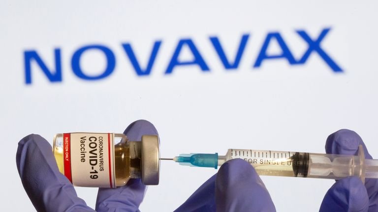 FILE PHOTO: Woman holds small bottle labeled with a "COVID-19 coronavirus vaccine" sticker and a medical syringe in front of the Novavax logo shown in this illustration