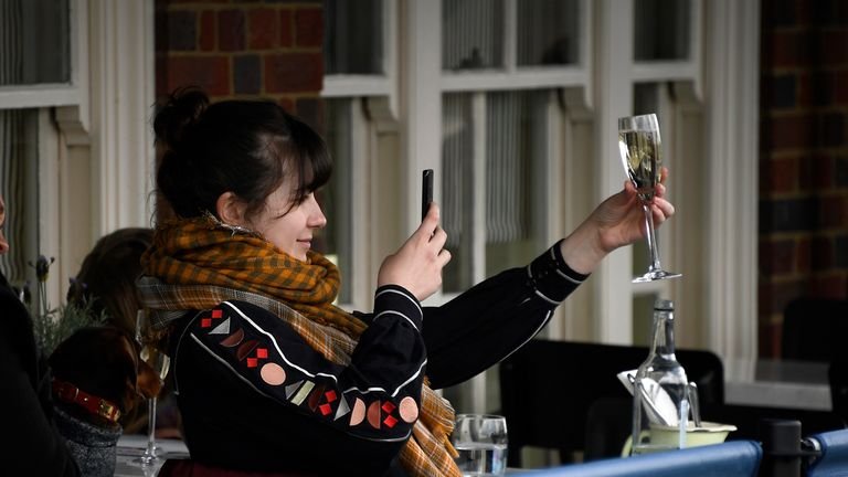 APTOPIX Virus Outbreak Britain A young woman takes a photo of her drink as she sits on a pub terrace in London on Monday, April 12, 2021. Millions of people in England will have their first chance in months for cuts of hair, occasional shopping and dining out on Monday, as the government takes the next step on its roadmap to lift the lockdown.  (AP Photo / Alberto Pezzali)