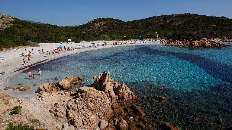 People stand at Ramizzo beach in what is called "Emerald Coast" from the island of Sardinia in Italy July 7, 2011