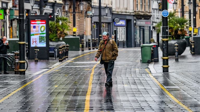 A man wears a face mask on his head in a nearly empty central shopping area in Cardiff, Wales, where they are on Alert Level 4 lockdown on the first weekend of the January sales, with many shops not open to navigation.